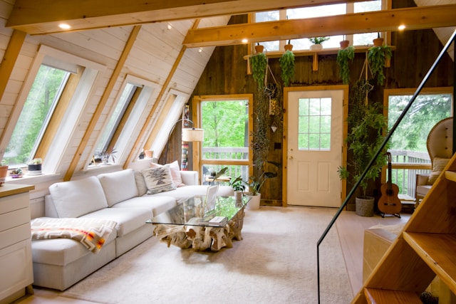 A cozy wooden room features a white sofa and a wooden table. The space is decorated with lush green plants, adding a touch of nature to the warm and inviting atmosphere